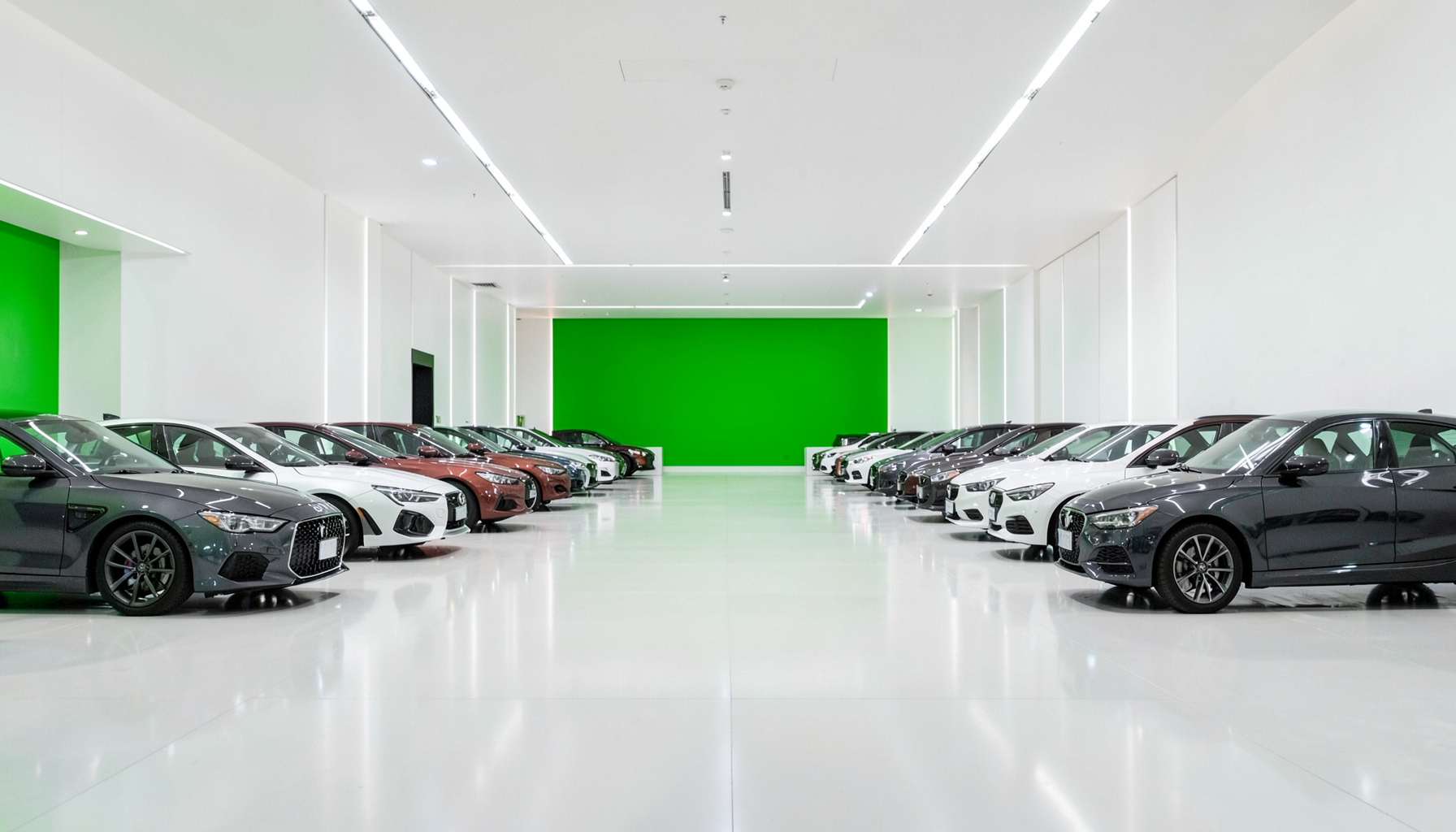 Geniş bir showroom içinde sıralanmış modern otomobiller, parlak zemin yansımaları ve tavandan gelen yumuşak beyaz ışıkla aydınlanan şık bir sergi alanı.